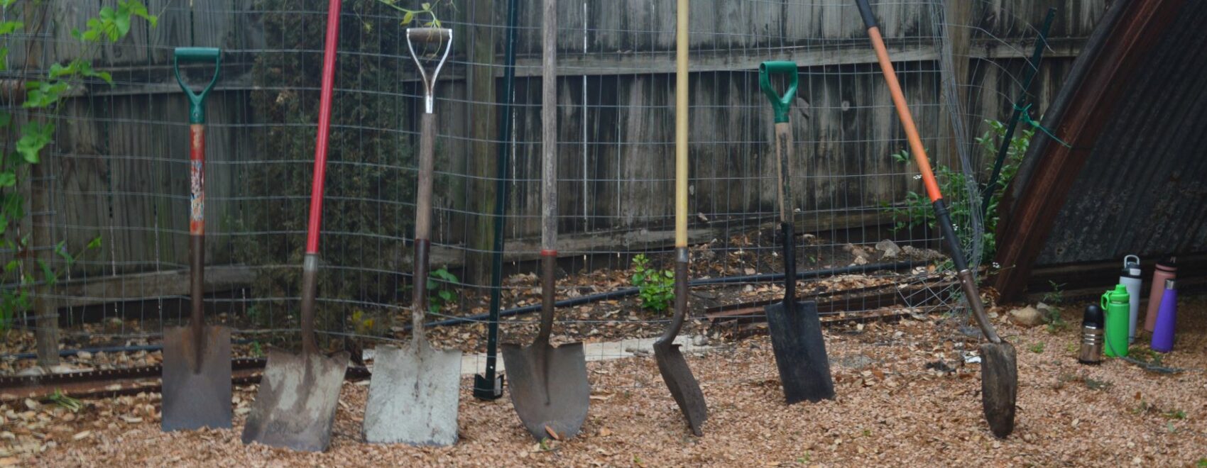 A line of shovels leaning against a wooden fence at The Eagle's Nest Community Garden at TecoloteSA.